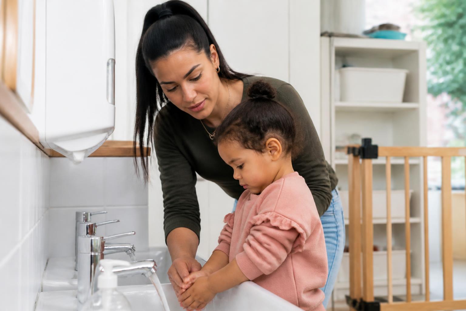 Pedagogisch medewerker helpt een kind bij het handen wassen aan de lage wasbak