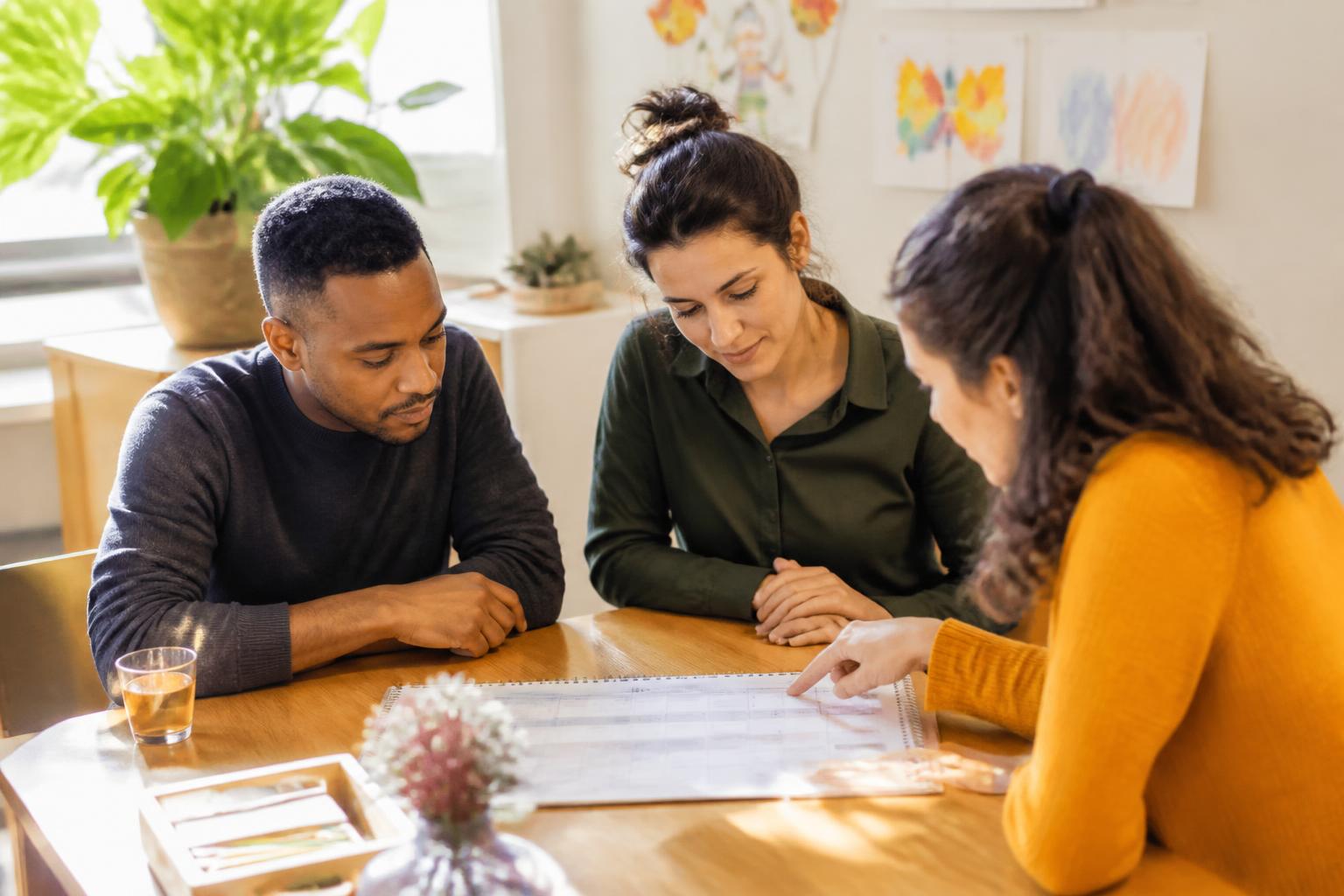 Twee ouders nemen samen met een medewerker de opvangkalender door aan tafel